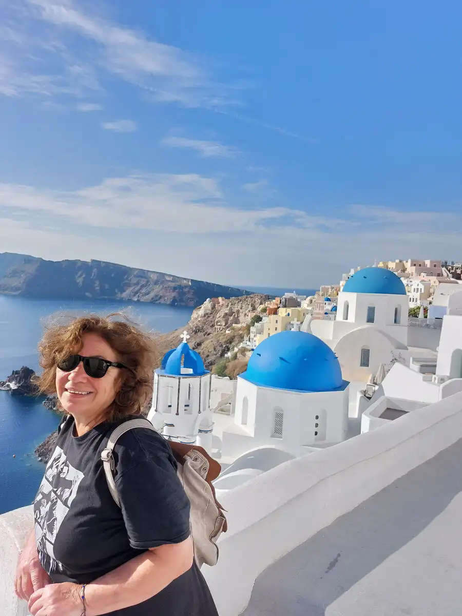 woman is photographed overlooking a traditional santorini white church with blue roofs and sea view.