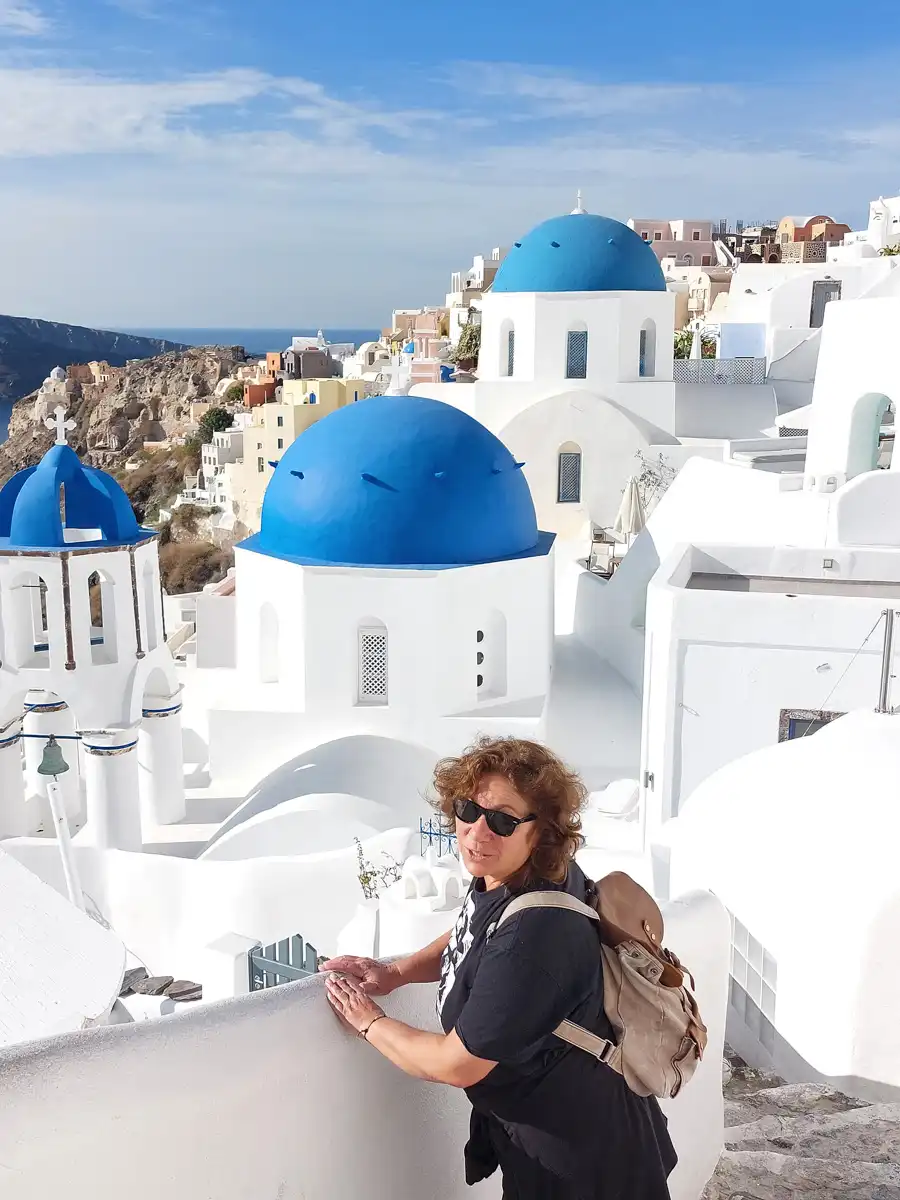 woman is photographed overlooking a traditional santorini white church with blue roofs