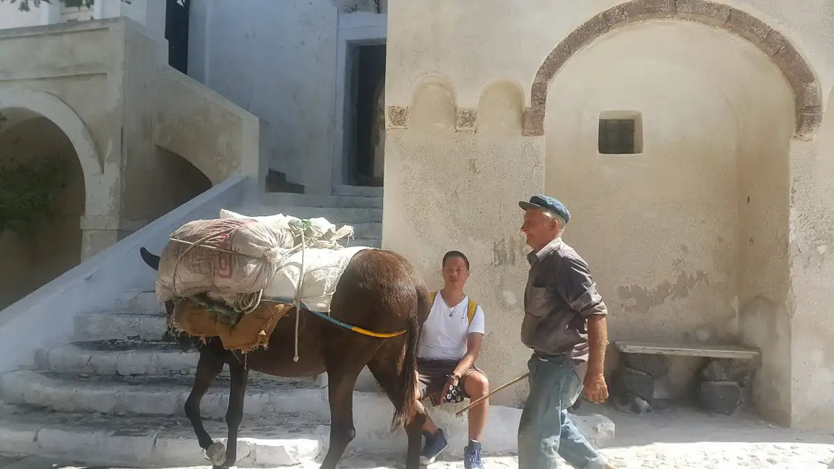 a local with his donkey and a tourist on a street in Santorini