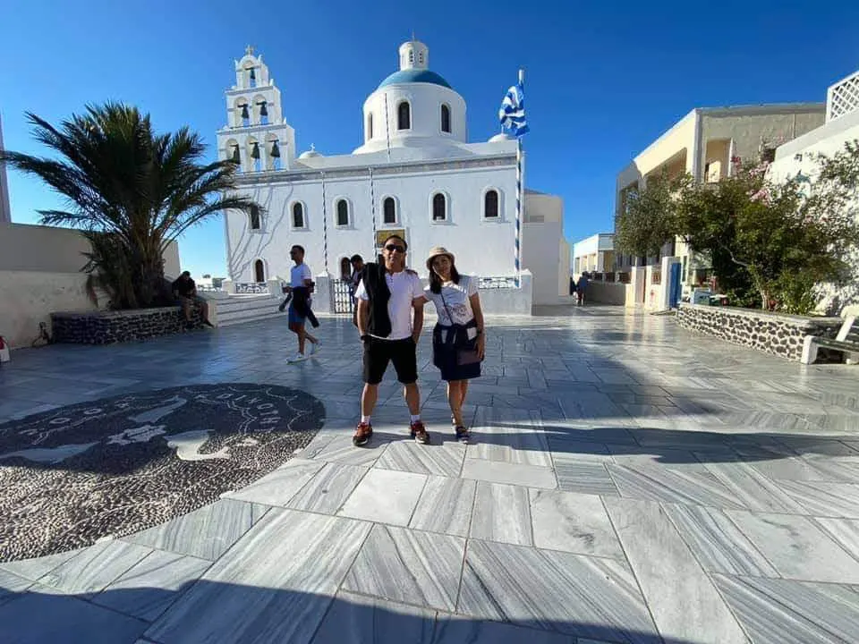 couple of tourists posing at the view of traditional church of santorini